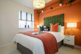 A cozy and vibrant bedroom with an orange accent wall, a plush bedding set, and a modern lighting fixture, creating a warm and inviting atmosphere.