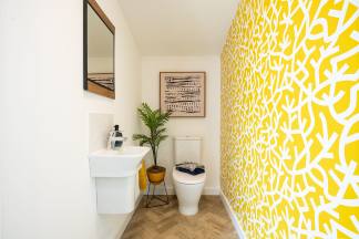 A small bathroom with a white toilet and sink, a potted plant, and a vibrant yellow and white patterned wallpaper covering the walls.