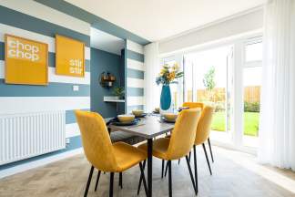 A modern and vibrant dining area with a wooden table, yellow upholstered chairs, and colorful wall decor, surrounded by large windows overlooking a lush outdoor space.