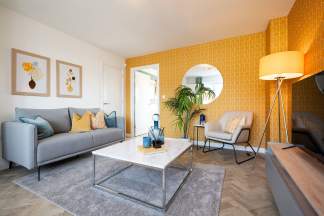 A cozy and vibrant living room with a gray sofa, yellow accent walls, and modern decor elements such as a glass-topped coffee table and framed artwork.