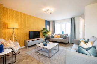 A cozy and vibrant living room with a yellow geometric-patterned accent wall, a gray sectional sofa, a glass-topped coffee table, and various decorative elements such as lamps and throw pillows.