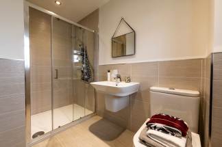 A modern bathroom features a glass-enclosed shower in the foreground and a toilet with folded towels in the background.