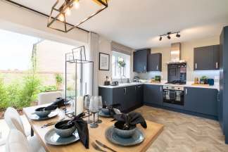 A dining table set for a meal sits in the foreground, with a modern kitchen featuring dark cabinets and stainless steel appliances in the background.