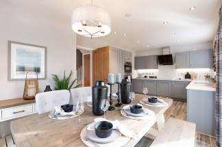 A modern and stylish kitchen with a dining area, featuring gray cabinets, wooden countertops, and a pendant light fixture, along with various decorative elements on the dining table.