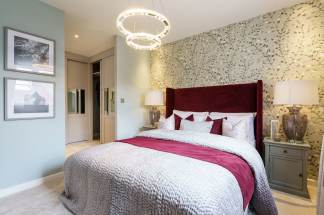 A plush bedroom features a burgundy headboard and a textured bedspread in the foreground, with a closet and patterned wallpaper in the background.