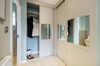 A modern closet with sliding doors and mirrored panels stands in a room with light blue walls and a plush carpet, while a glimpse of a bathroom is visible in the background.