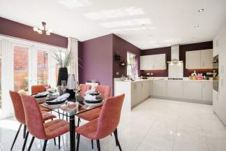 A glass-top dining table with coral chairs sits in the foreground, while a modern kitchen with light-colored cabinets and a purple accent wall occupies the background.