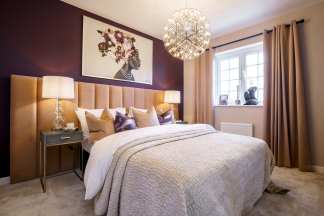 A plush bed with a textured quilt and decorative pillows sits in the foreground, while a large abstract portrait hangs above the headboard against a deep purple wall in the background.