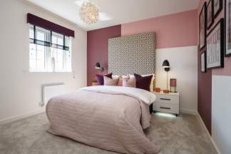A plush pink comforter covers a bed in the foreground, while the background features a wall painted in alternating shades of pink and white, adorned with framed artwork.