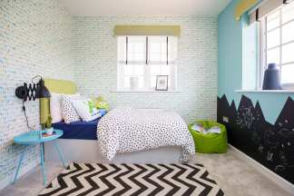 A child's bedroom features a bed with playful bedding in the foreground, while the background showcases a window with blinds and walls adorned with alphabet wallpaper and a mountain mural.