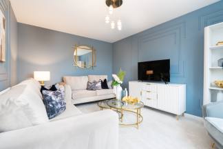A modern living room features a white sofa in the foreground and a blue accent wall with a television and decorative molding in the background.