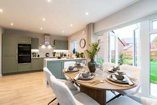A modern and well-appointed kitchen with a dining area, featuring a wooden table set with place settings and surrounded by comfortable chairs, all set against a backdrop of large windows overlooking a garden.