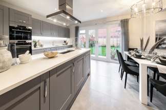 A modern, well-designed kitchen with gray cabinets, a white countertop, and a dining area with black chairs, all illuminated by a chandelier and natural light from the windows.