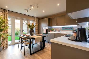A modern kitchen with a dining table set for a meal in the foreground and a view of a green backyard through glass doors in the background.
