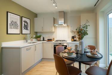 A modern kitchen with a dining table set for a meal in the foreground and a sleek, L-shaped countertop with appliances in the background.
