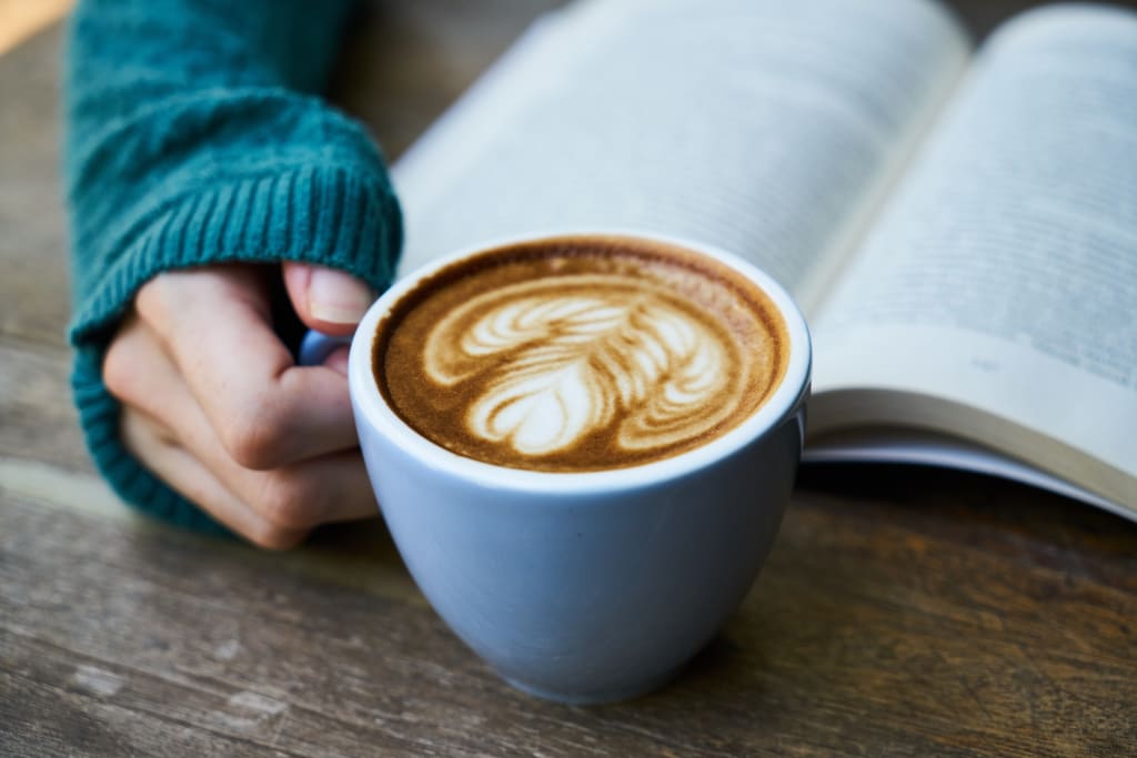 blue sweatered hand holding warm latte in front of book wondering Should I Hire an Editor for My First Book?