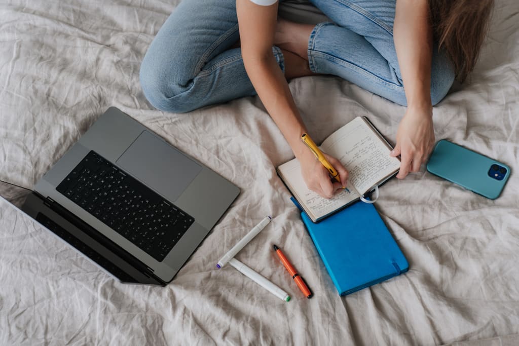 person on bed with laptop phone notebook finding where to submit short stories