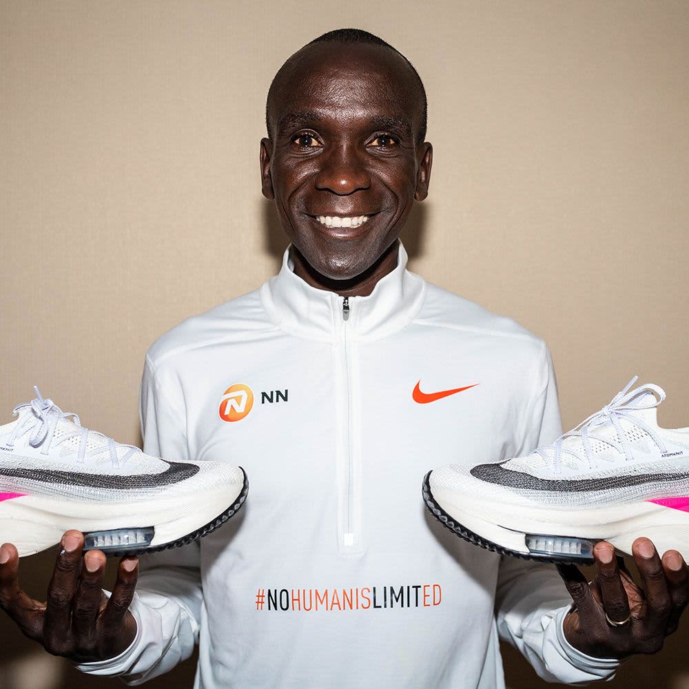 Eliud Kipchoge holding running shoes in each hand