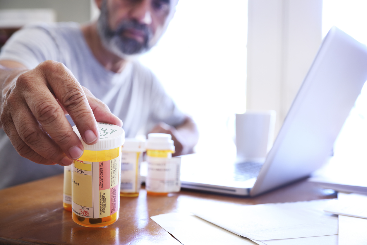 Man sitting at a laptop sorting medication bottles