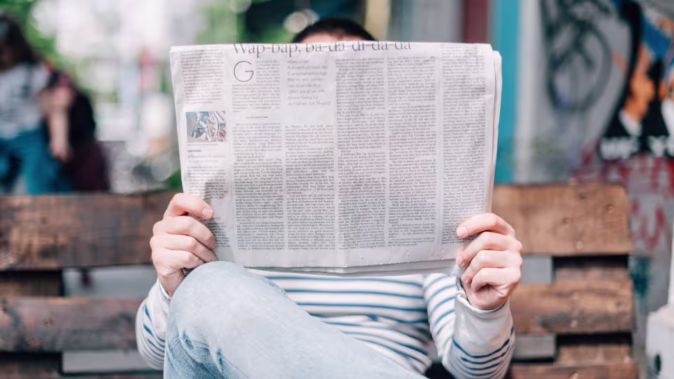 person sitting on a park bench reading the latest news