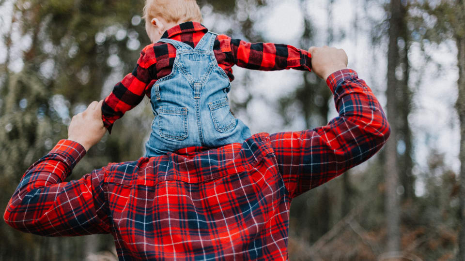 A father giving a biggy back ride to a young child in the park