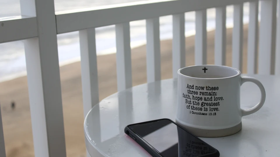 A coffee mug and cell phone on a patio table overlooking the ocean