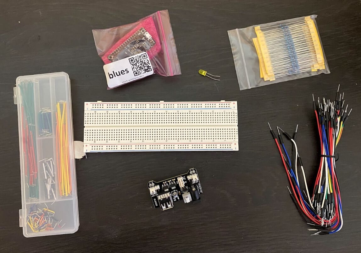 work surface holds the project components including an empty breadboard, a power source, a Swan development board from Blues, an LED, and various jumper wires and other basic components