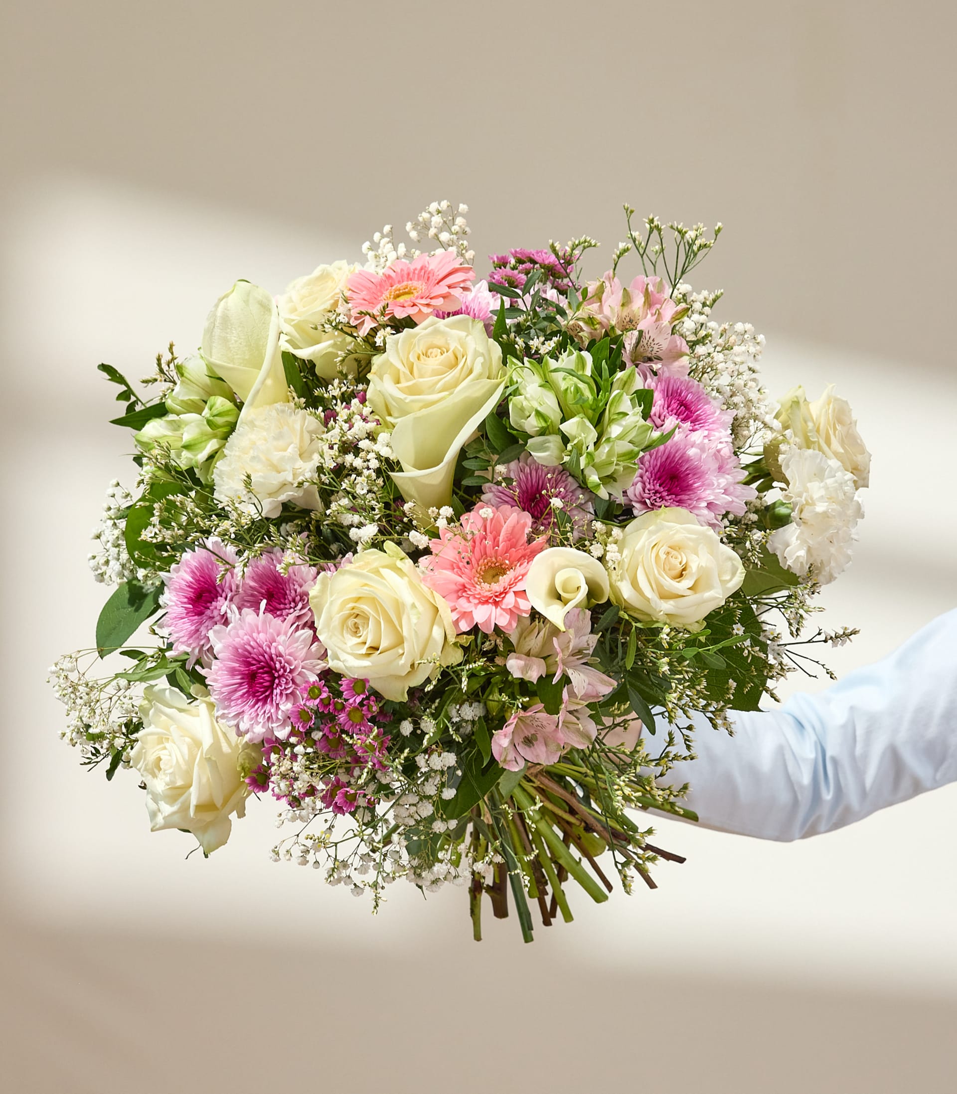 Ein lebendiger Strauß verschiedener Blumen, darunter rosa Gerbera, weiße Rosen und zartes Schleierkraut, vor einem sanften blauen Hintergrund.