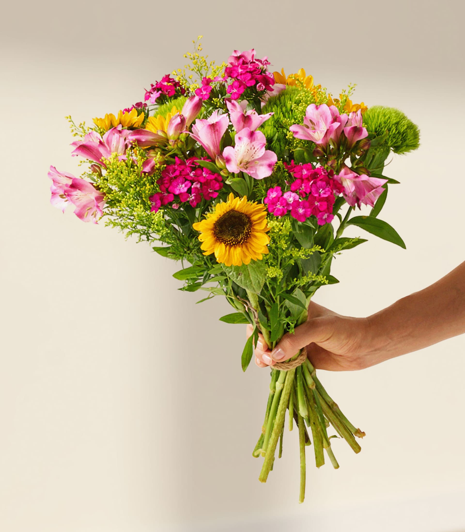 Ein farbenfroher Strauß aus Sonnenblumen, rosa Blumen und Grünpflanzen, arrangiert in einer Glasvase vor einem schlichten weißen Hintergrund.