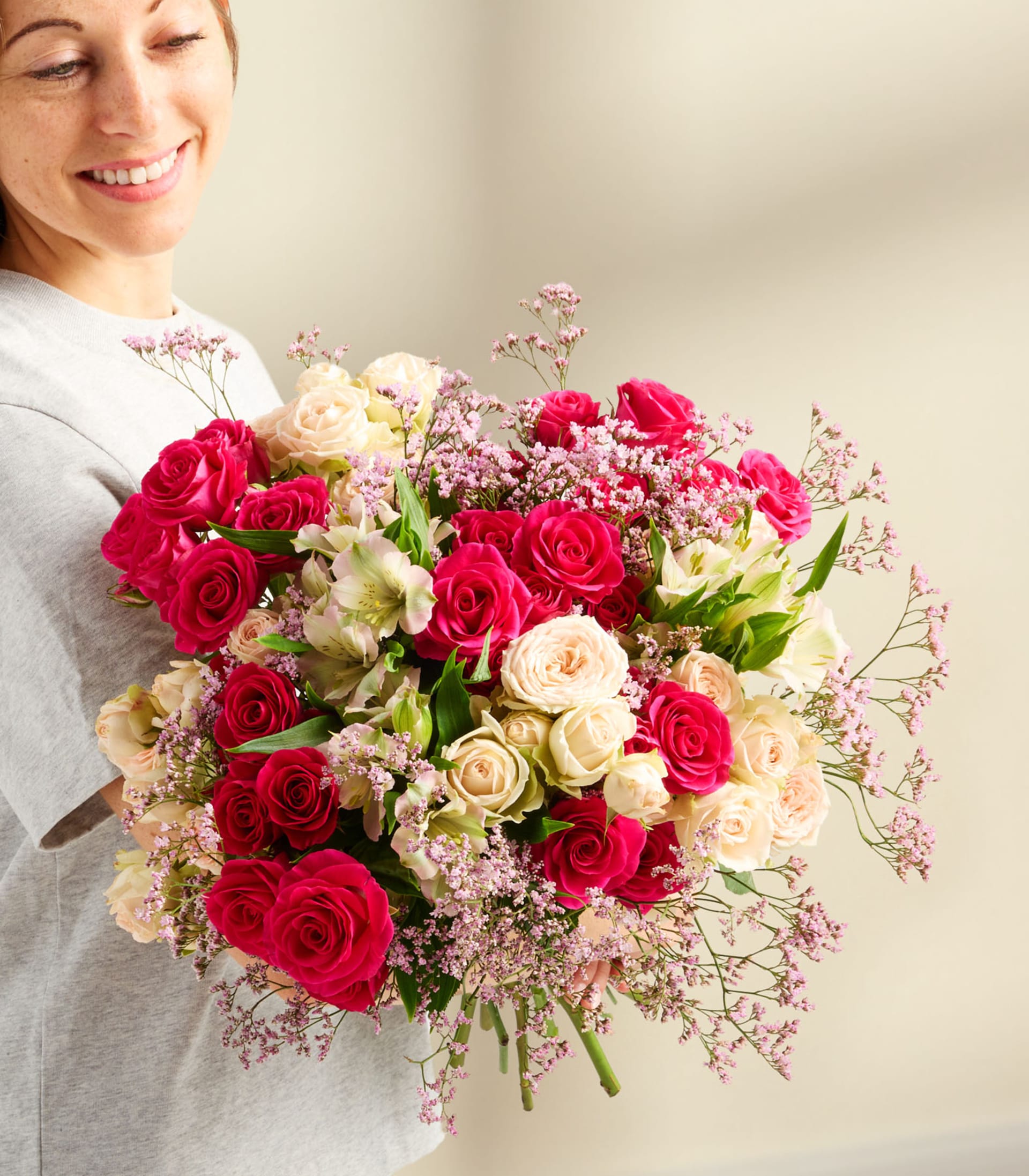 Ein farbenfroher Strauß roter und weißer Rosen, Nelken und anderer Blumen in einer Glasvase. Eine Hand greift hinein, um das Arrangement vor einem schlichten weißen Hintergrund zurechtzurücken.