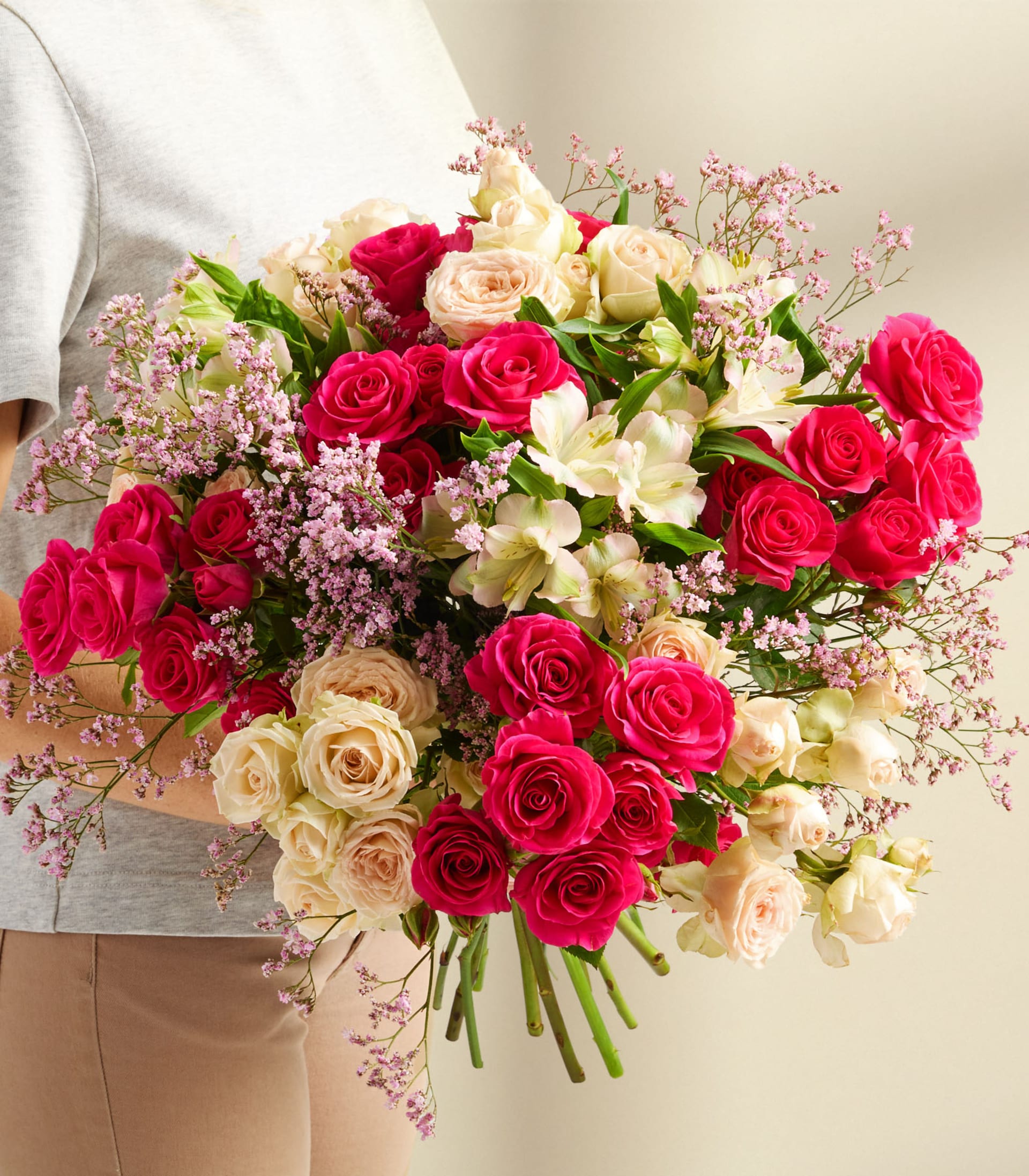 Ein farbenfroher Strauß verschiedener Blumen, darunter rote Rosen, rosa Nelken und weiße Lilien, arrangiert in einer klaren Glasvase vor einem schlichten weißen Hintergrund.