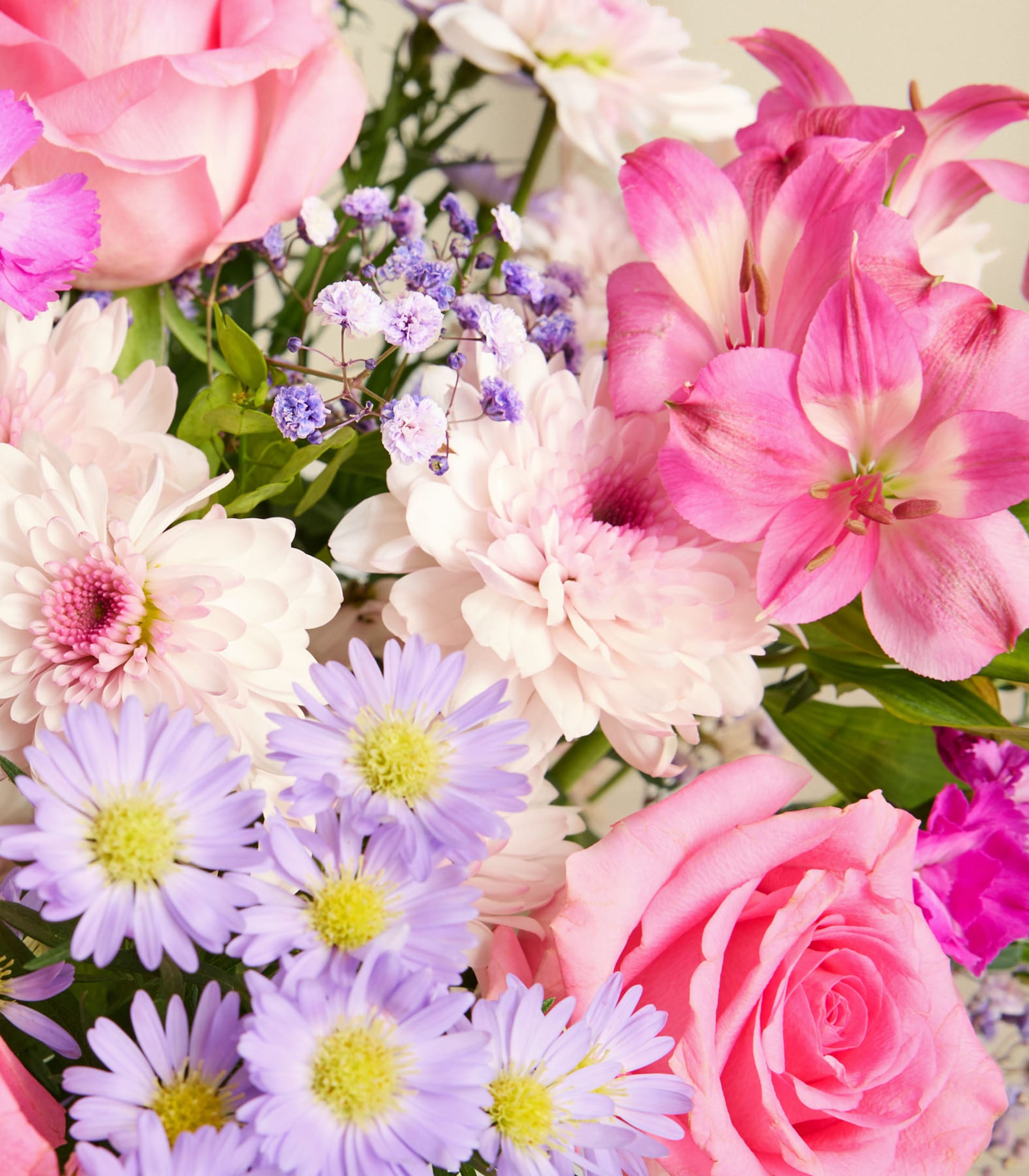 Ein lebendiger Strauß aus rosa Rosen, lila Gänseblümchen und anderen bunten Blumen, arrangiert in einer Glasvase vor einem schlichten weißen Hintergrund.