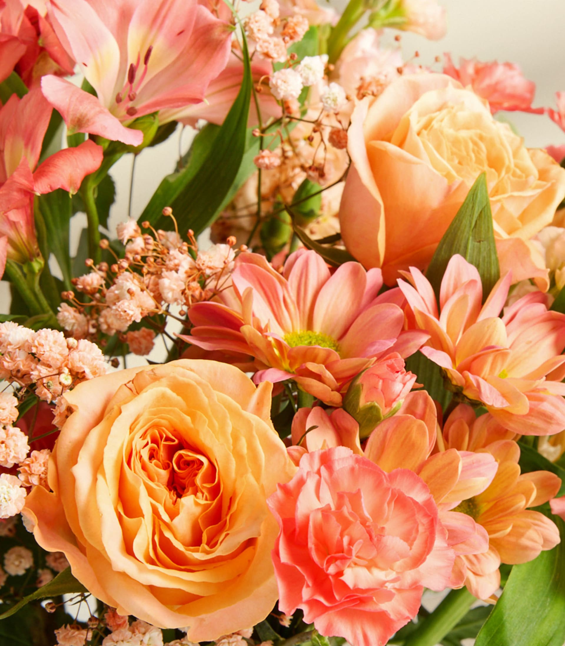 Ein farbenfroher Strauß verschiedener Blumen, darunter Rosen, Gänseblümchen und andere Blüten in Rosa-, Orange- und Gelbtönen, vor einem weichen, unscharfen Hintergrund.