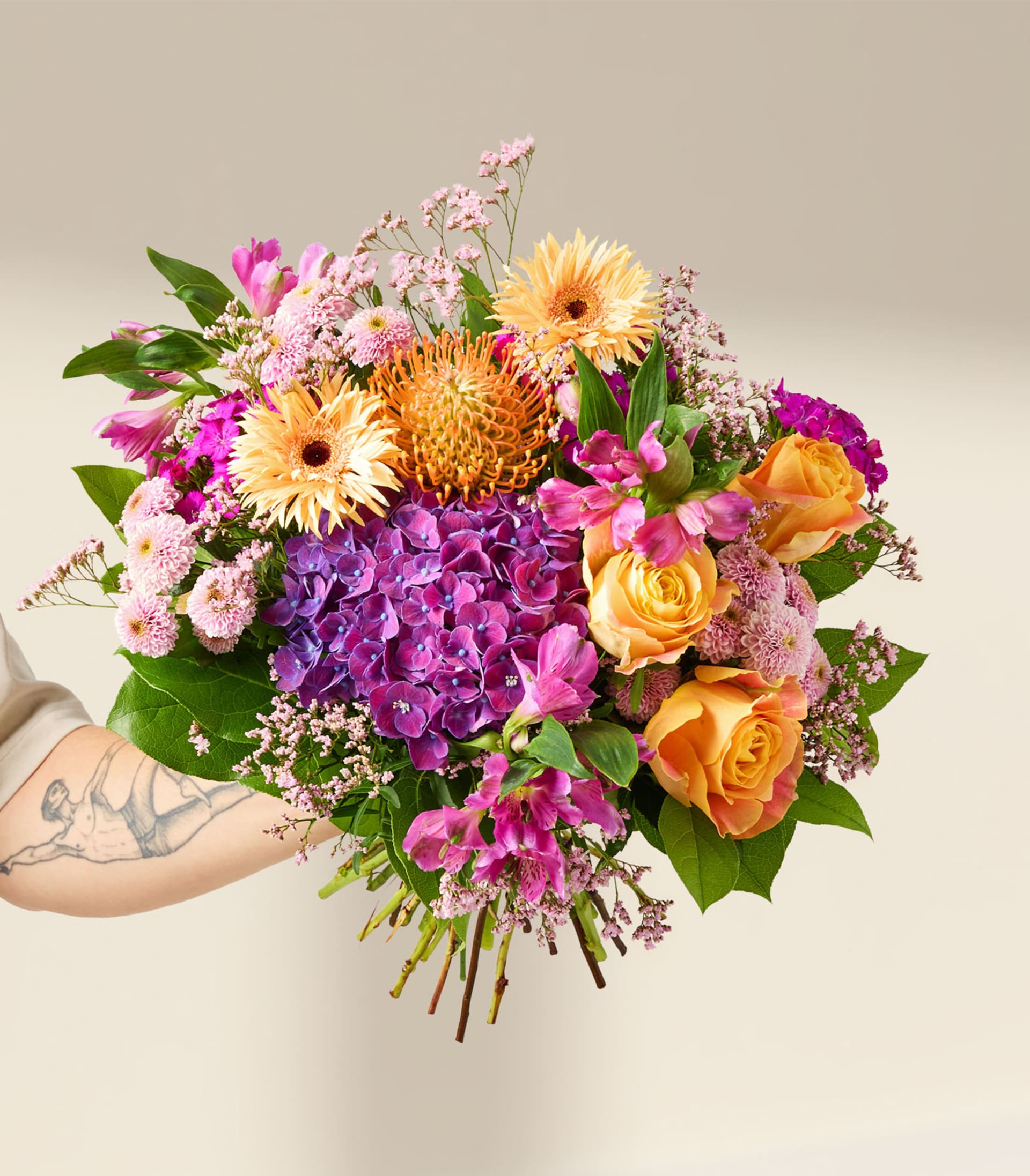 Ein lebendiger Strauß bunter Blumen, darunter rosa Hortensien, gelbe Rosen und eine große Sonnenblume, vor einem üppigen grünen Hintergrund.