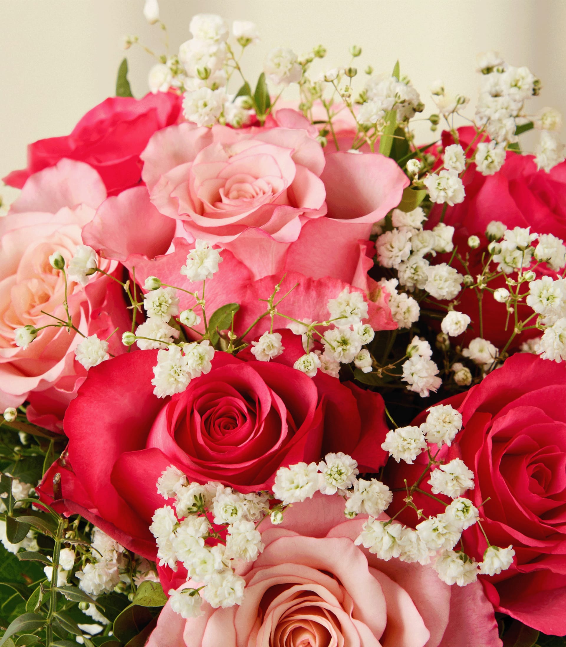 Eine Hand hält einen wunderschönen Strauß leuchtend rosa und roter Rosen, Schleierkraut und anderer zarter Blumen, die in einer Glasvase vor einem schlichten, hellen Hintergrund arrangiert sind.