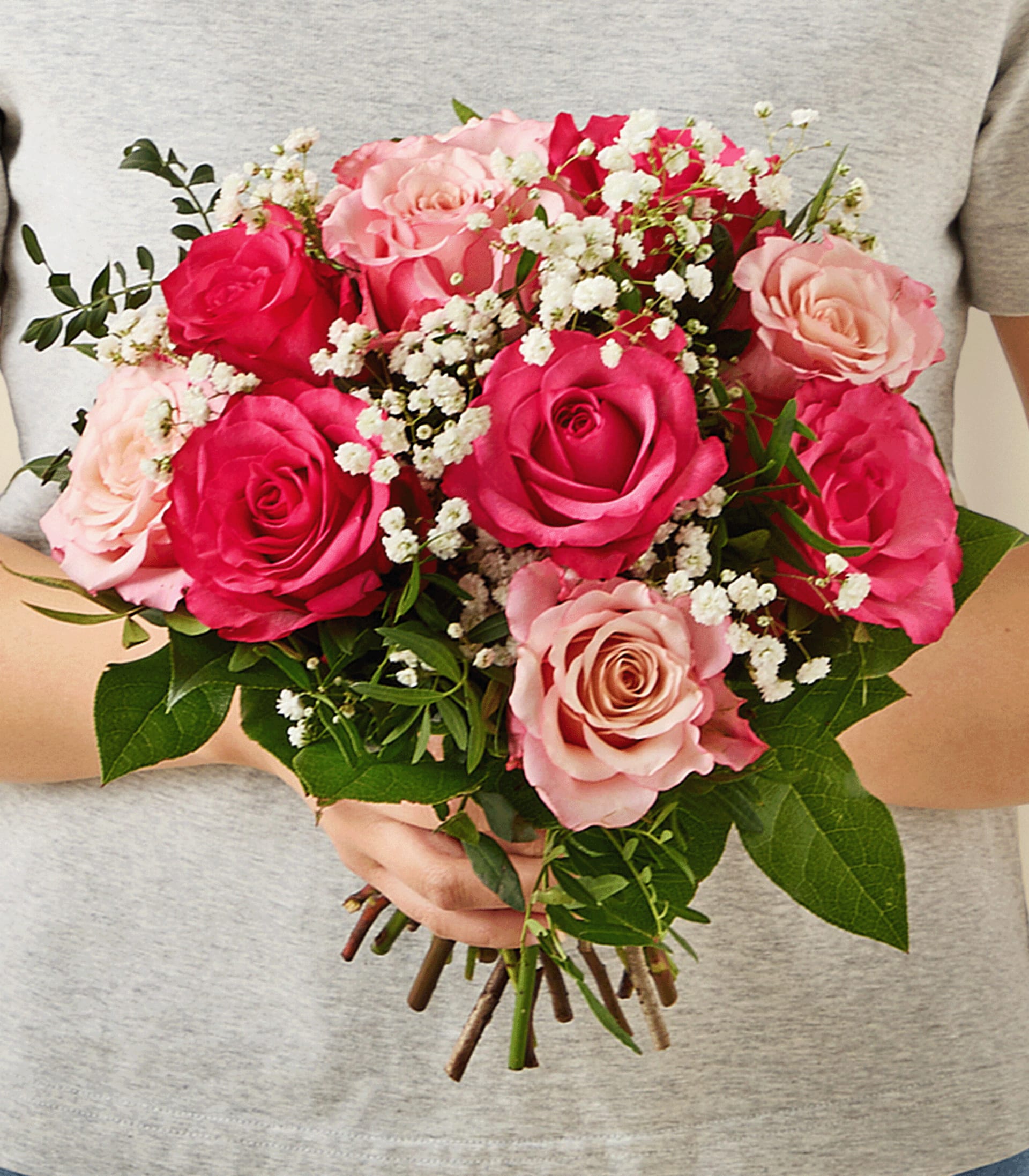Ein Strauß leuchtend roter Rosen, zartrosa Nelken und kleiner weißer Blumen in einer Glasvase steht auf einer schlichten, hellen Oberfläche.