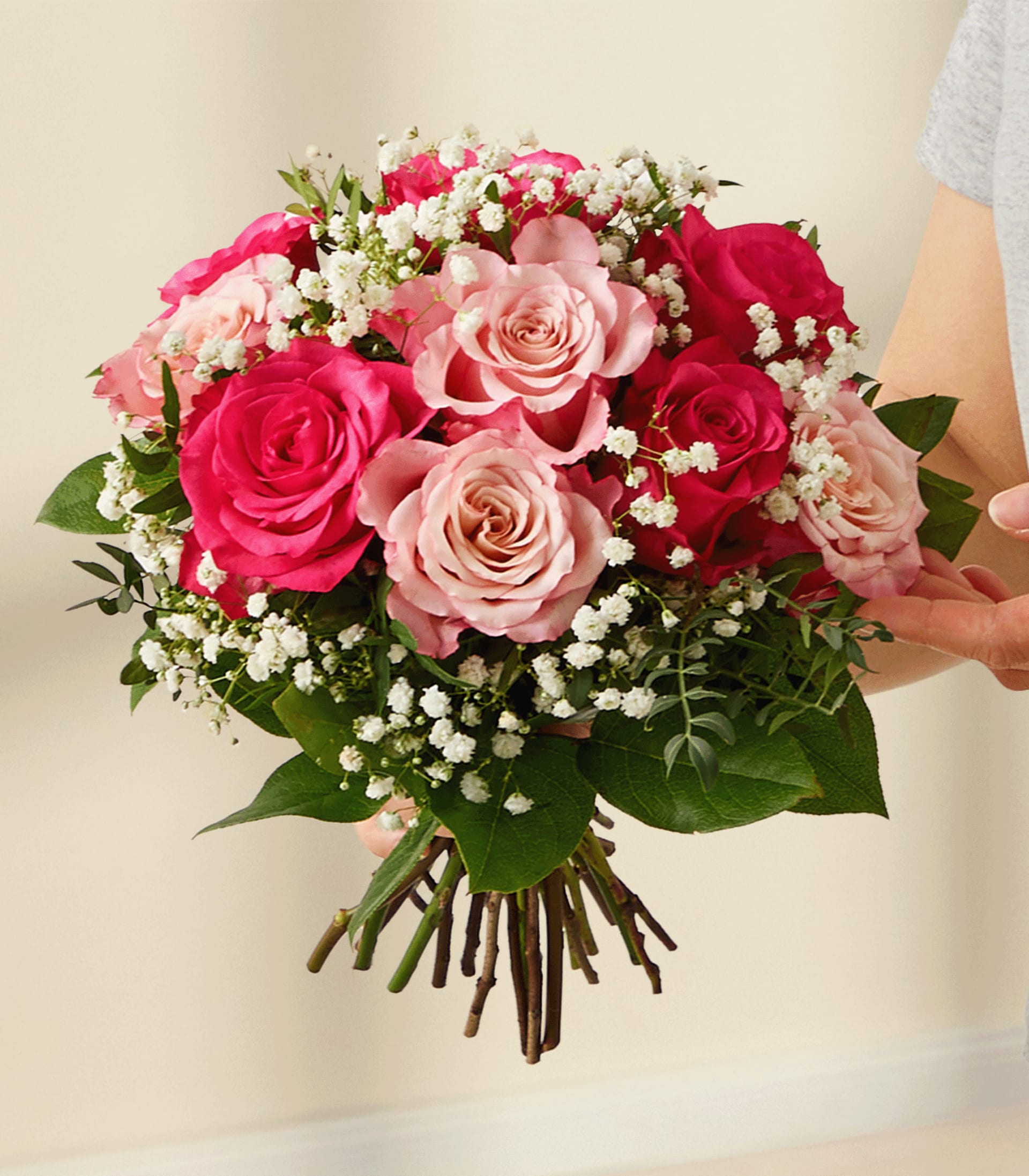 Eine junge Frau in einem hellen Hemd hält einen Strauß leuchtend rosa Rosen und anderer Blumen vor einem schlichten weißen Hintergrund.