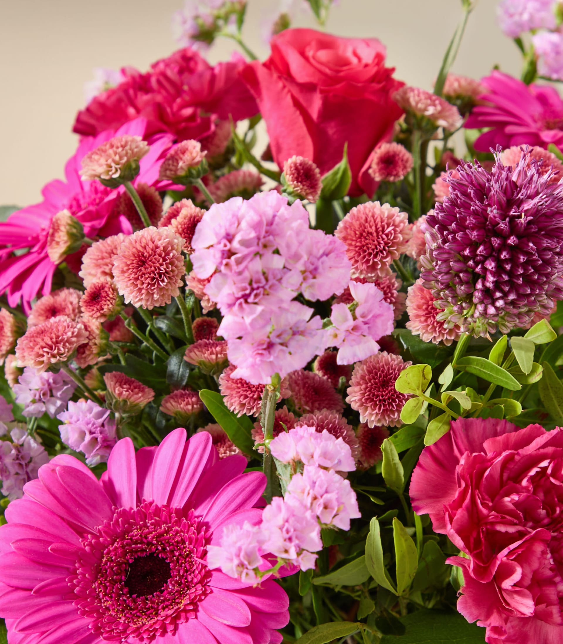 Ein lebhafter Strauß aus rosa und roten Blumen, darunter Rosen, Gerbera und Nelken, hebt sich von einem sanften, neutralen Hintergrund ab.