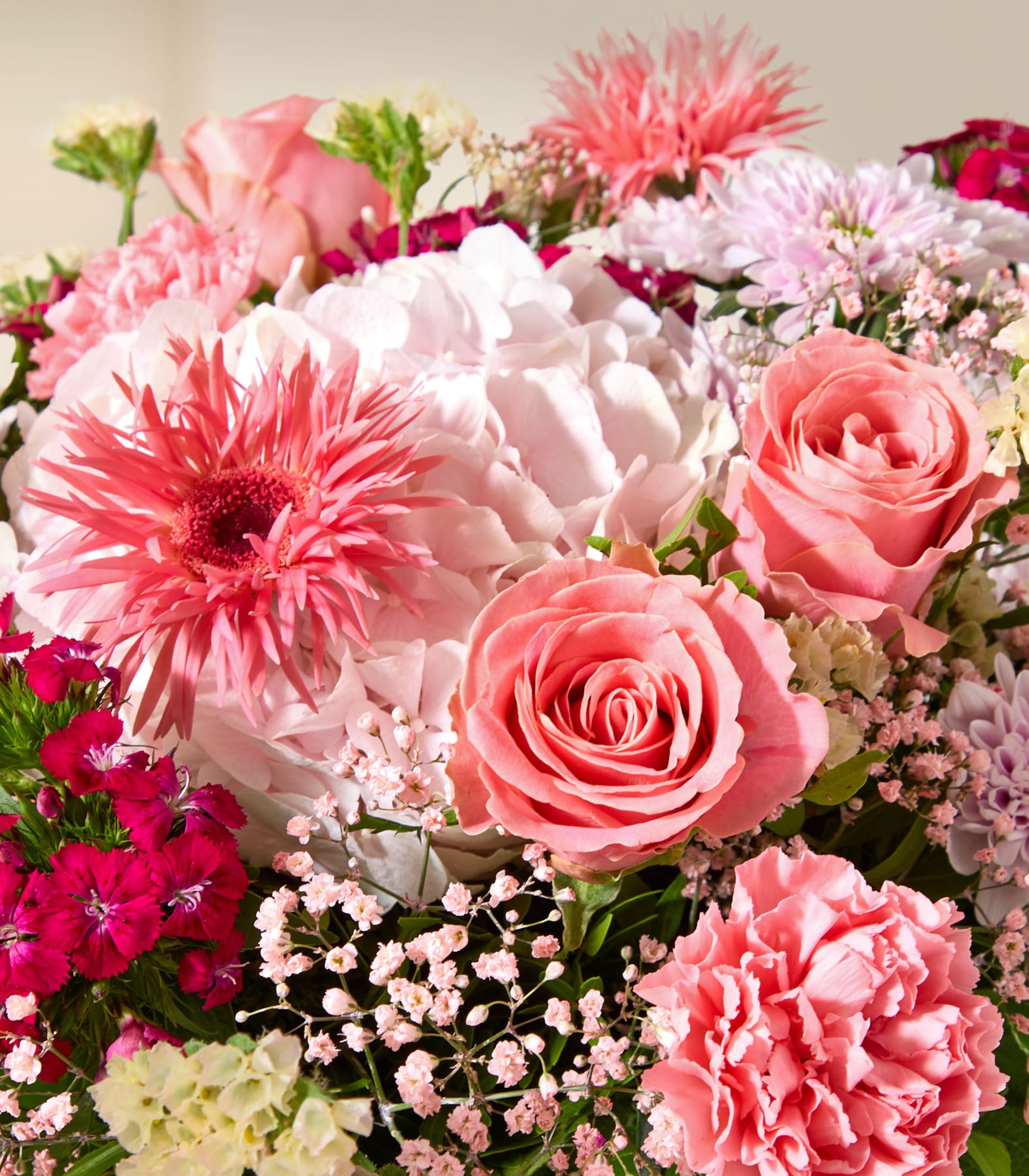 Ein lebhafter Strauß aus rosa und weißen Blumen, darunter Rosen, Nelken und Gerbera-Gänseblümchen, ist vor einem weichen, verschwommenen Hintergrund arrangiert.