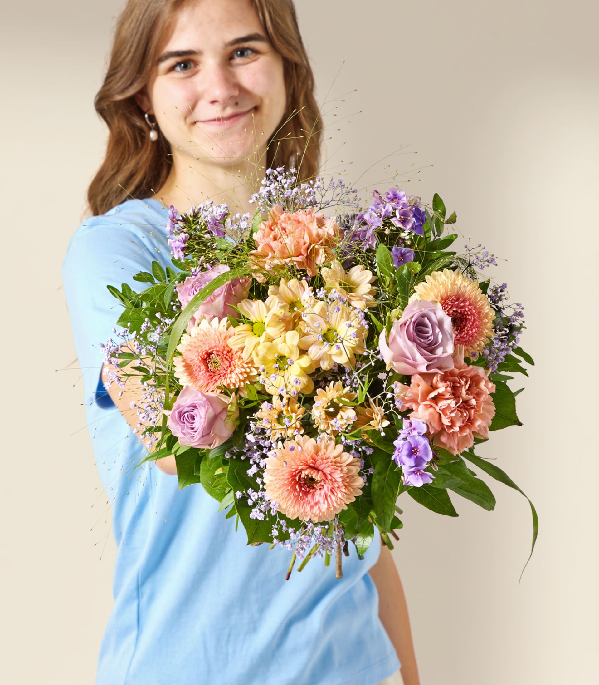Eine junge Frau in einem blauen Hemd hält einen farbenprächtigen Strauß bunter Blumen vor einem schlichten, hellen Hintergrund.