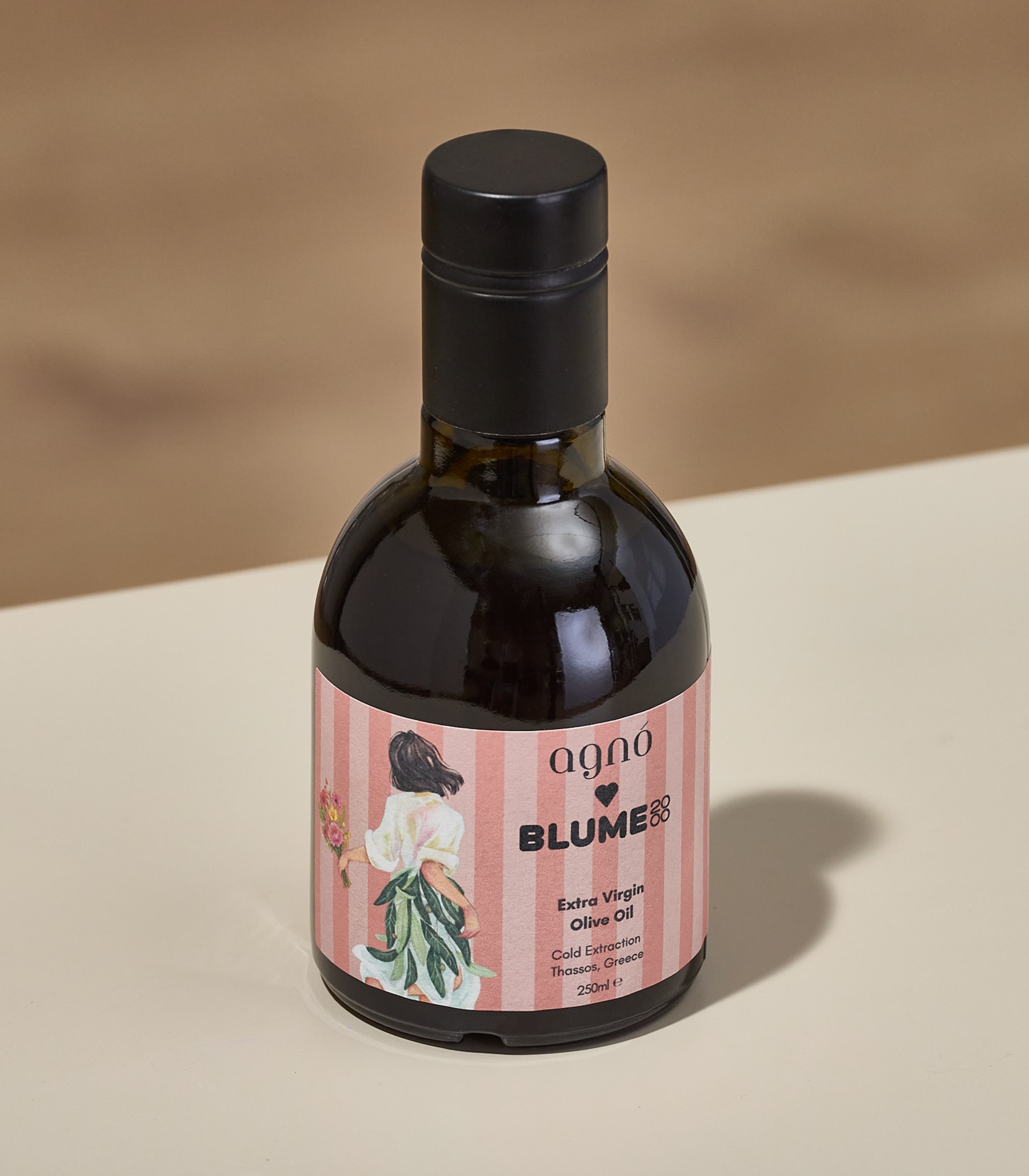 Eine Flasche Agno natives Olivenöl extra mit schwarzem Verschluss steht auf einer hellen Oberfläche vor einem verschwommenen Holzhintergrund.