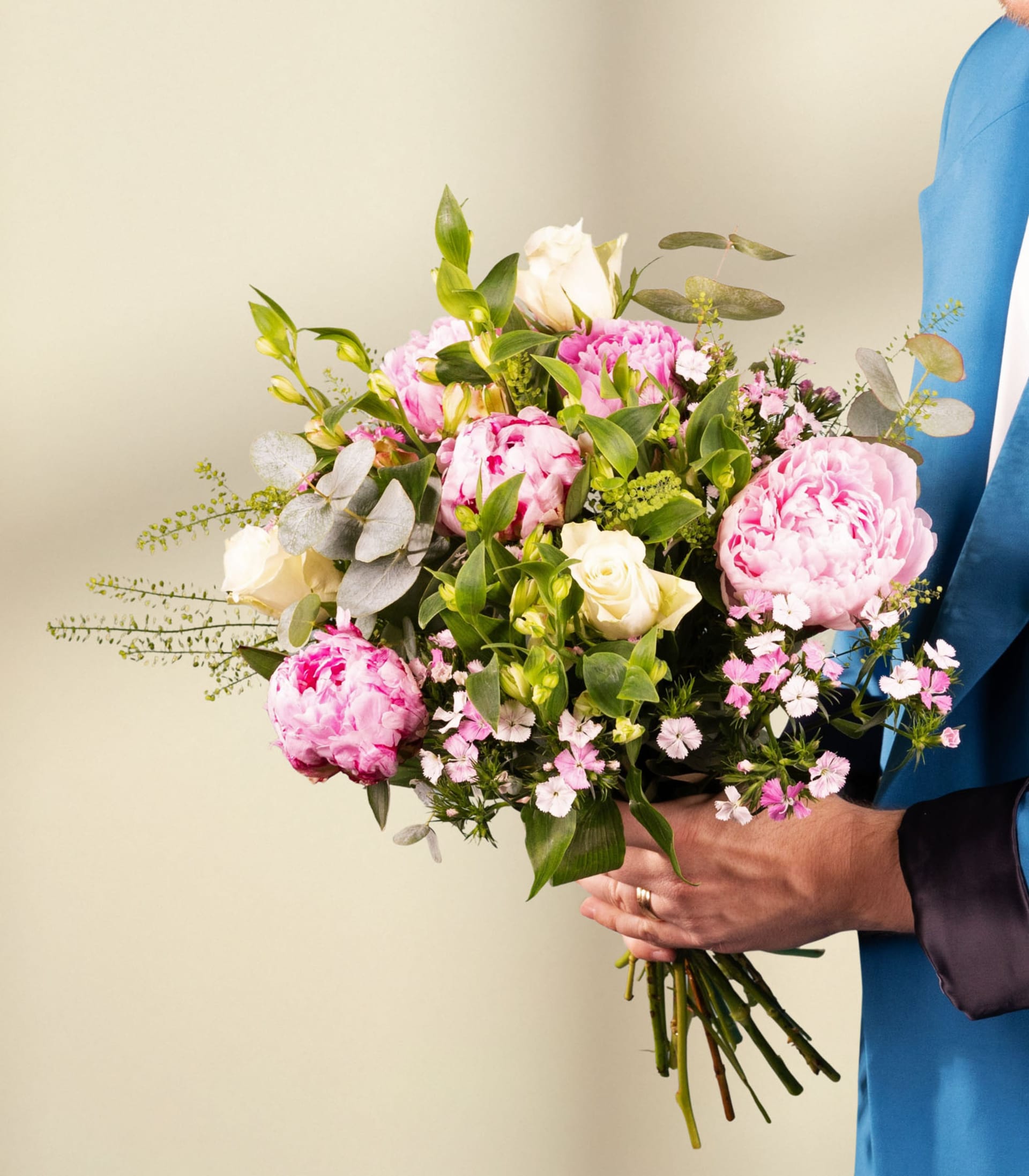 Ein wunderschöner Strauß rosa und weißer Blumen, darunter Pfingstrosen und Rosen, arrangiert in einer Glasvase vor einem schlichten weißen Hintergrund.