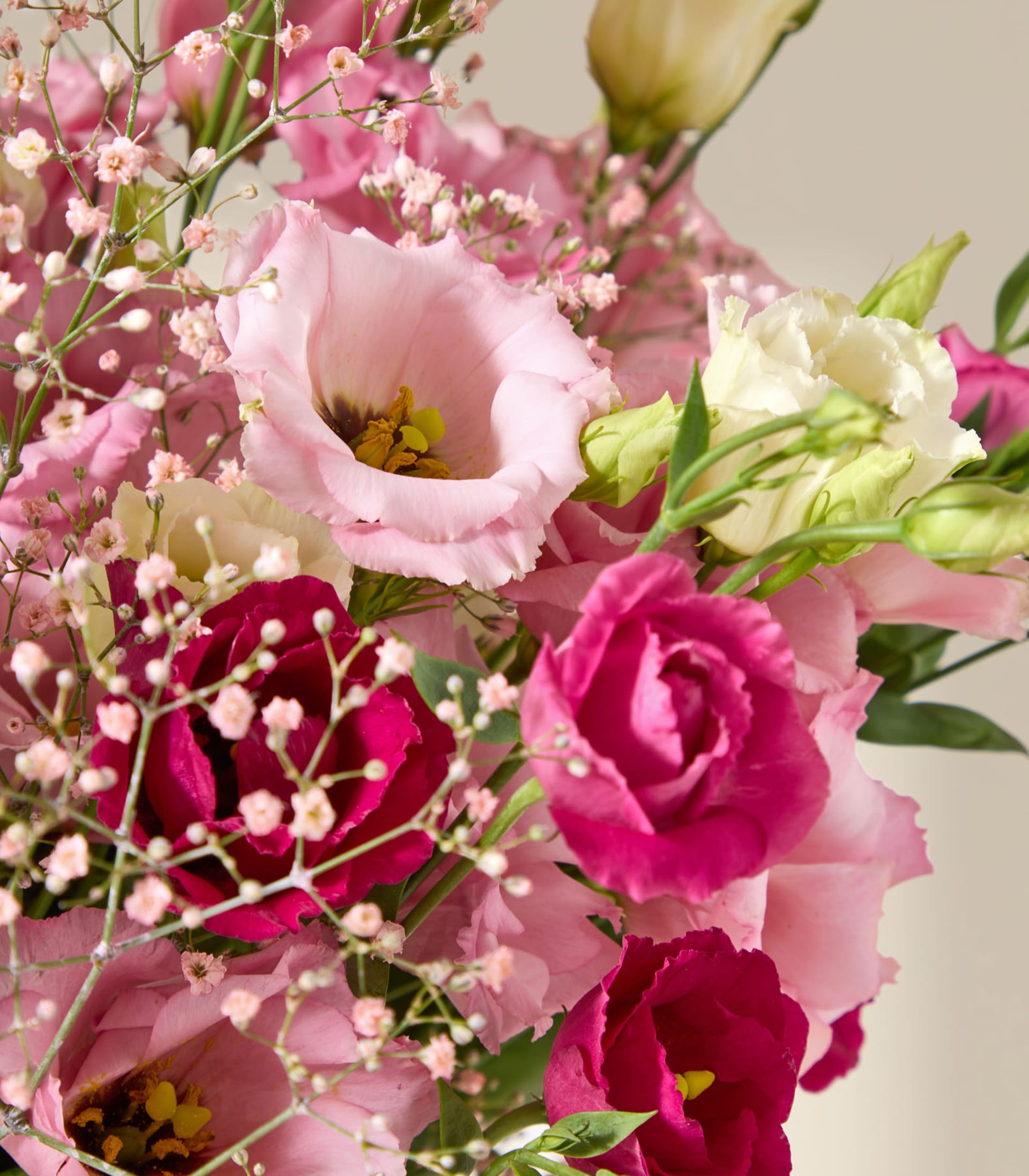 Eine lächelnde Frau in einem weißen Hemd hält einen großen Strauß rosa und weißer Blumen vor einem schlichten Hintergrund.