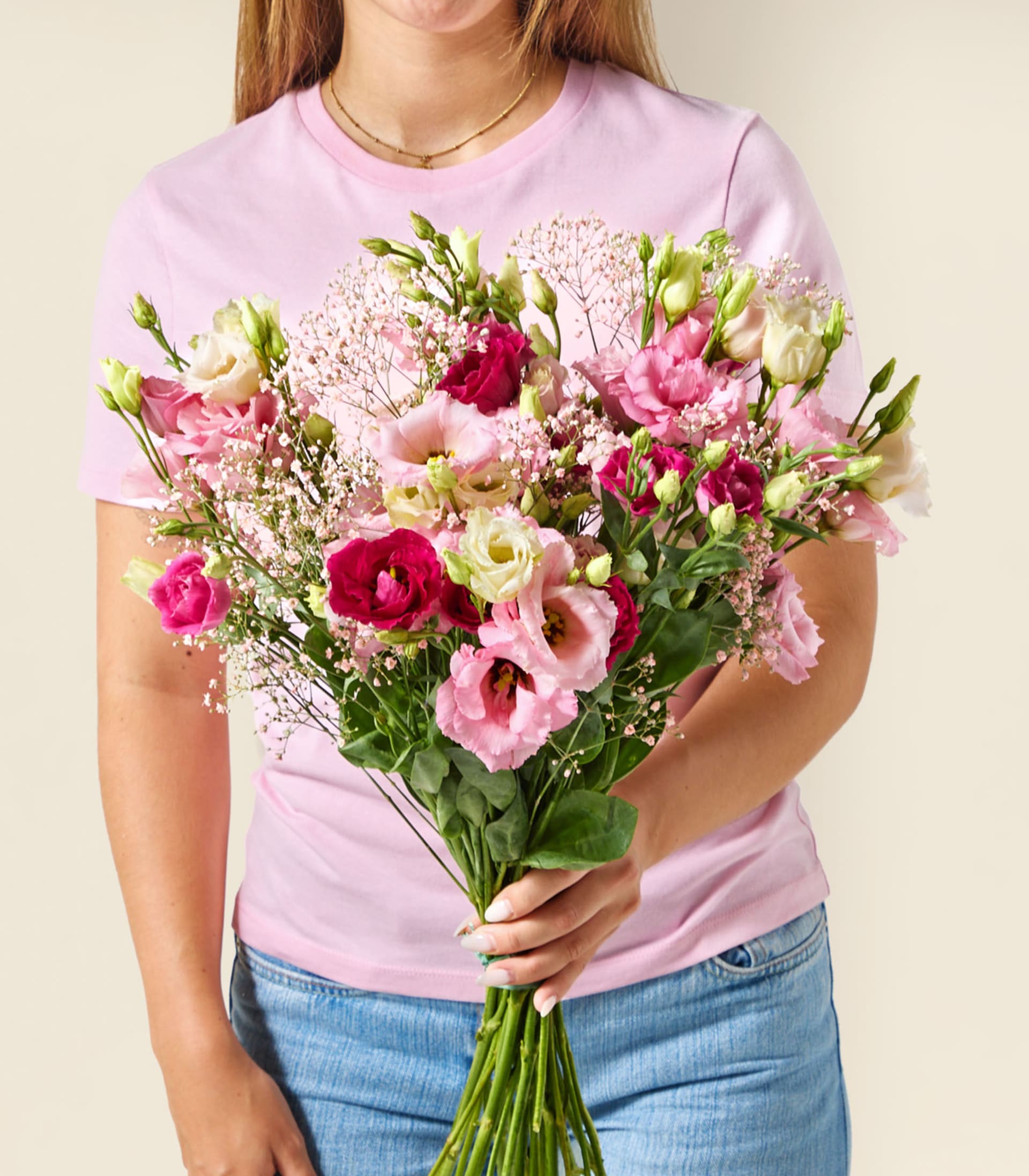 Ein farbenfroher Strauß verschiedener rosa, roter und weißer Blumen, darunter Rosen, Lisianthus und Schleierkraut, wird vor einem schlichten weißen Hintergrund in den Händen einer Person gehalten.