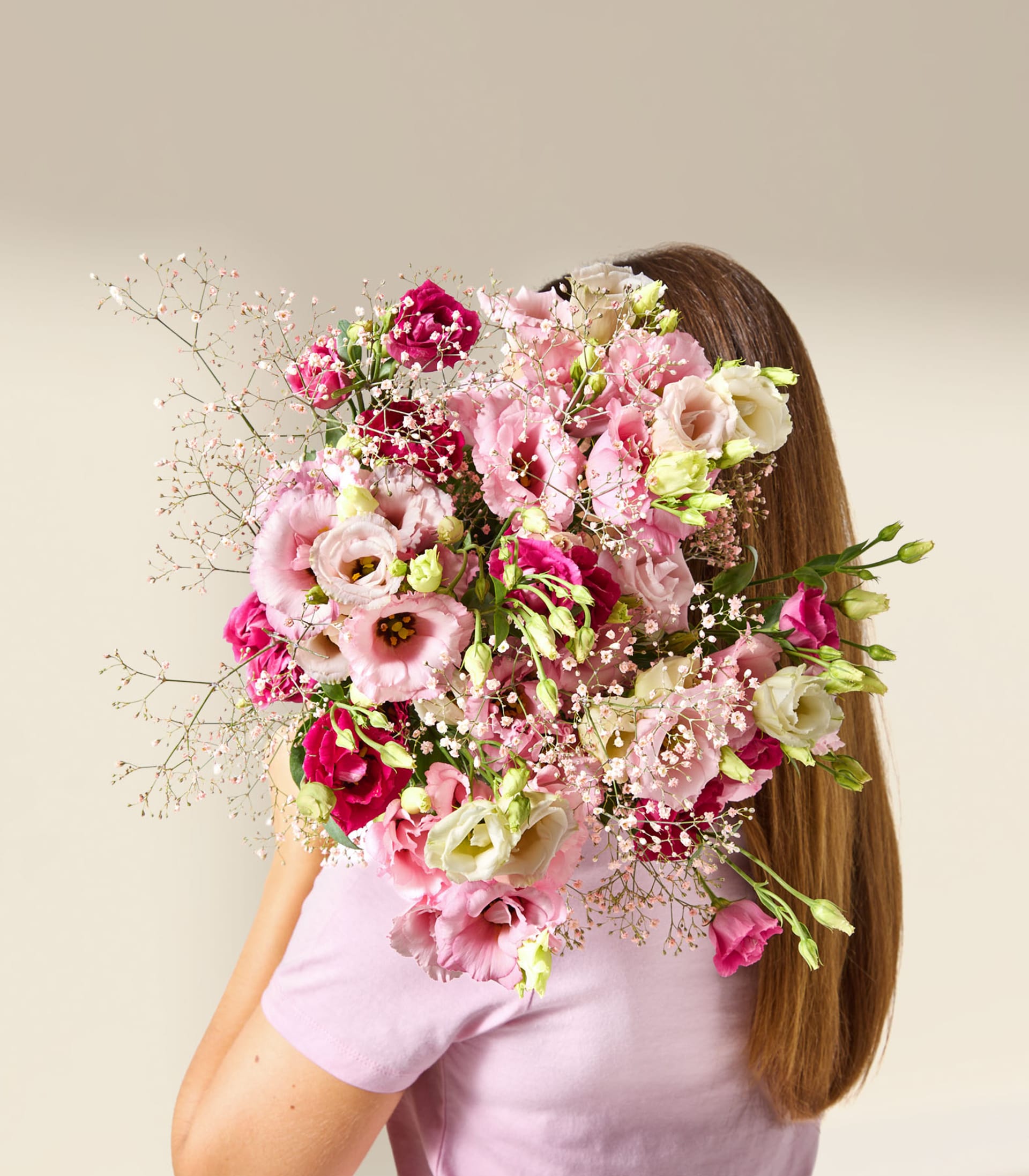Eine junge Frau mit langen blonden Haaren hält vor einem schlichten weißen Hintergrund einen Strauß bunter Blumen, darunter rosa und rote Rosen.