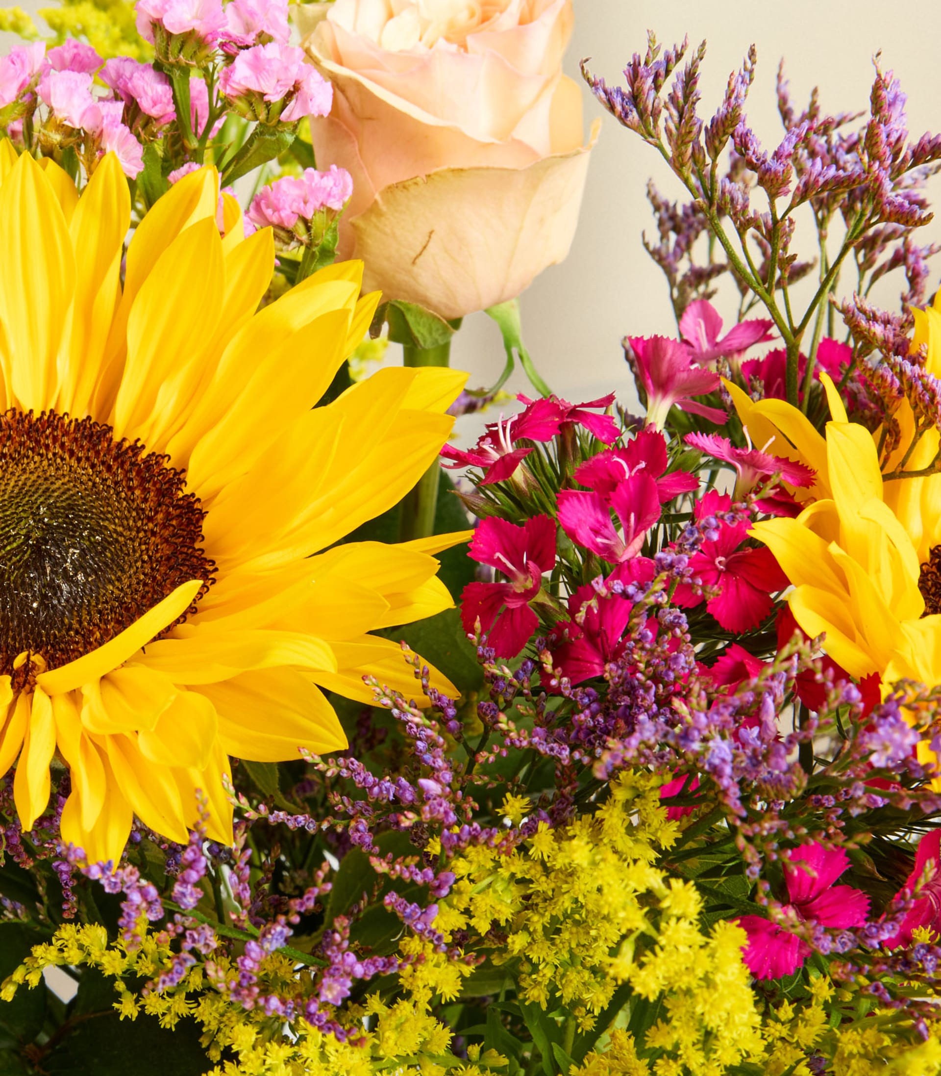 Ein lebendiger Strauß aus Sonnenblumen, Rosen und anderen bunten Blumen vor dem Hintergrund eines sanften blauen Himmels.