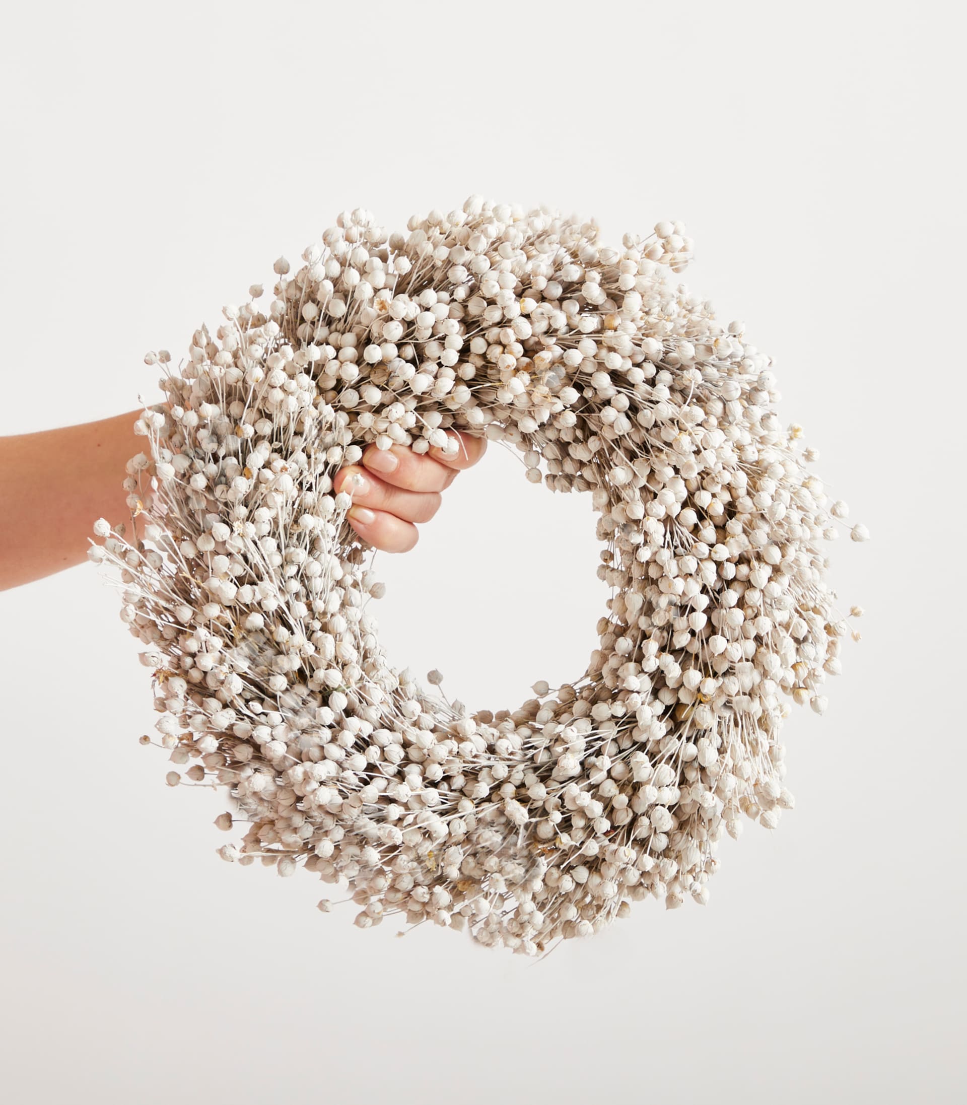 Vor einem schlichten weißen Hintergrund wird ein Kranz aus zarten weißen Wattestäbchen in den Händen gehalten.