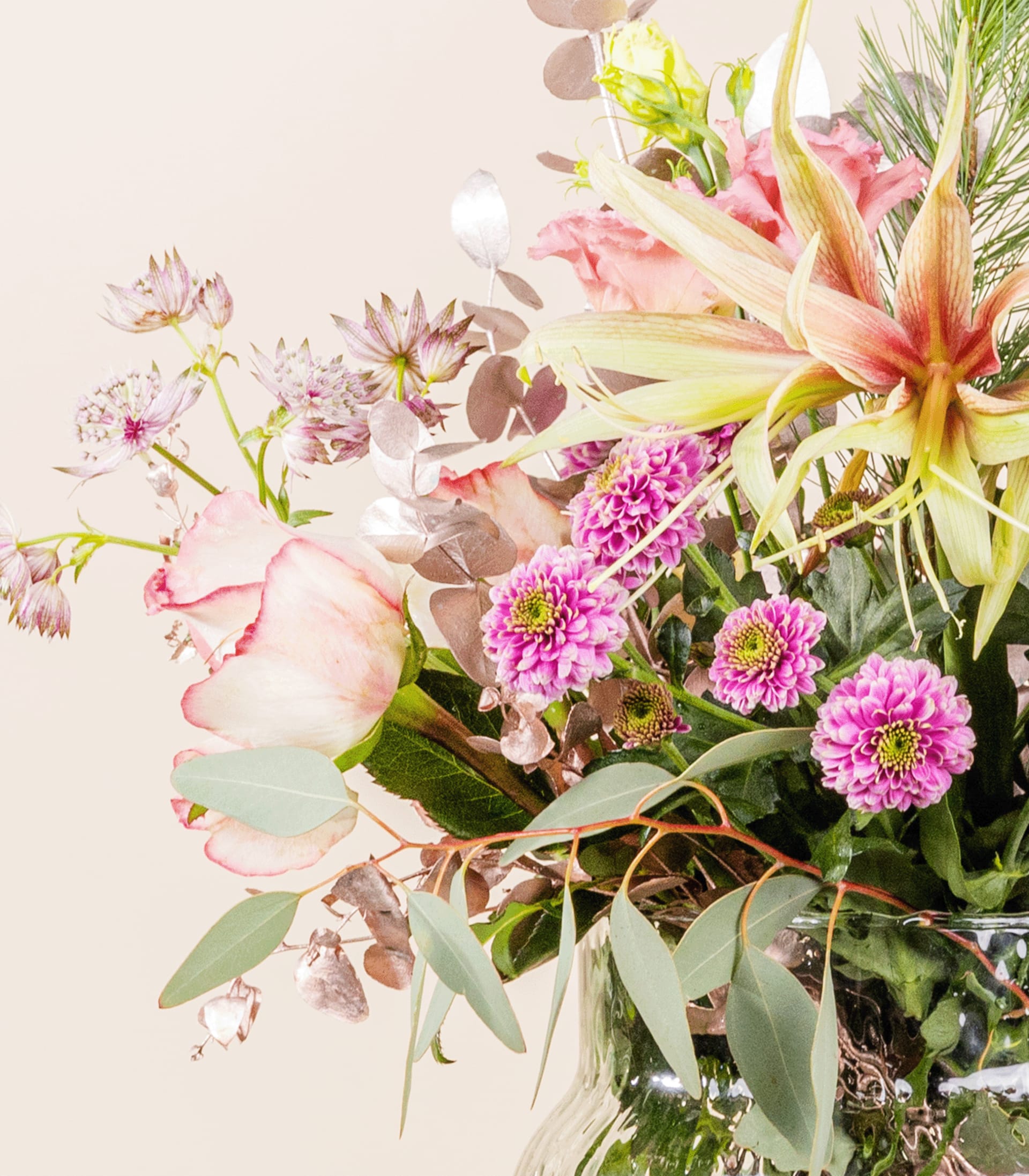 Ein lebendiger Strauß bunter Blumen, darunter rosa Dahlien, weiße Lilien und üppiges Grün, vor einem weichen, neutralen Hintergrund. (Beschreibungstext KI-generiert)