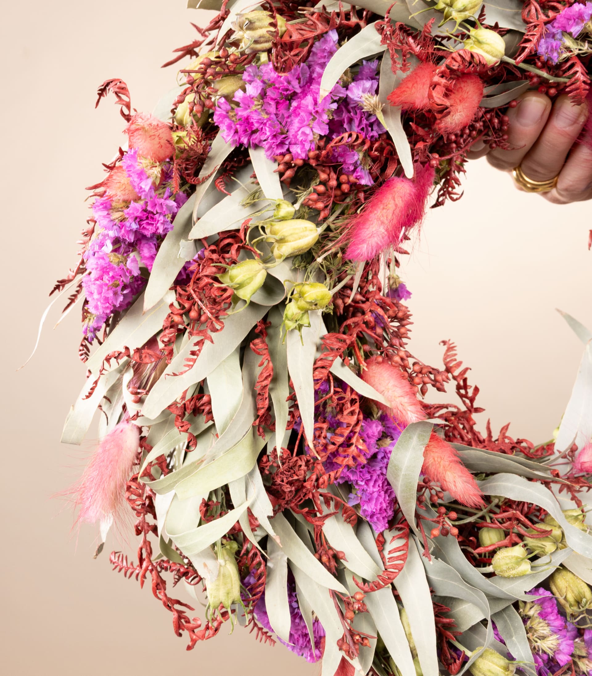 Jemand hält vor einem neutralen Hintergrund ein lebendiges und farbenfrohes Blumenarrangement mit einer Mischung aus rosa, roten und weißen Blumen sowie verschiedenen Grünpflanzen in den Händen.