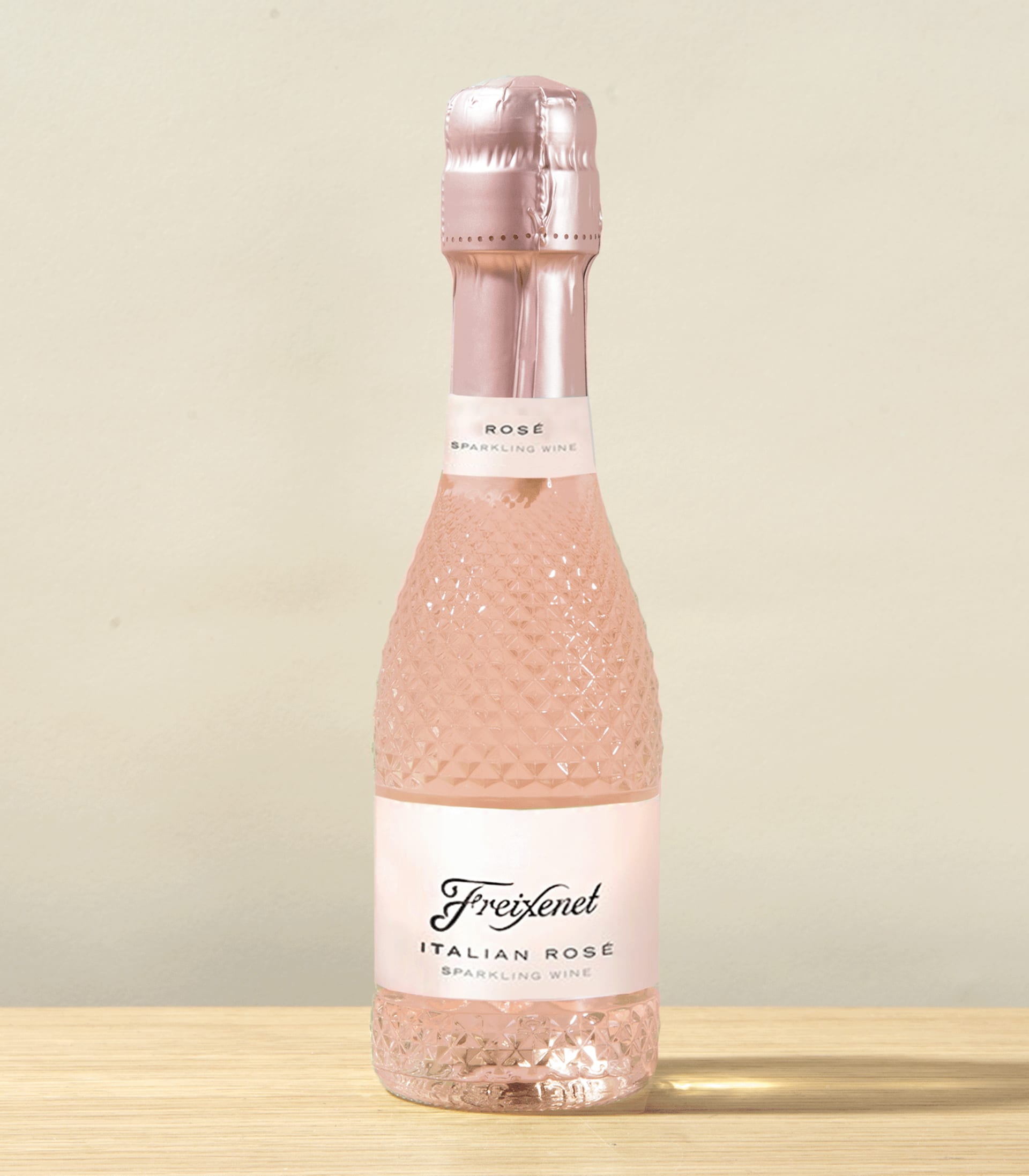 Eine rosafarbene, prickelnde Flasche italienischen Roséweins steht auf einer Holzoberfläche vor einem hellen Hintergrund.